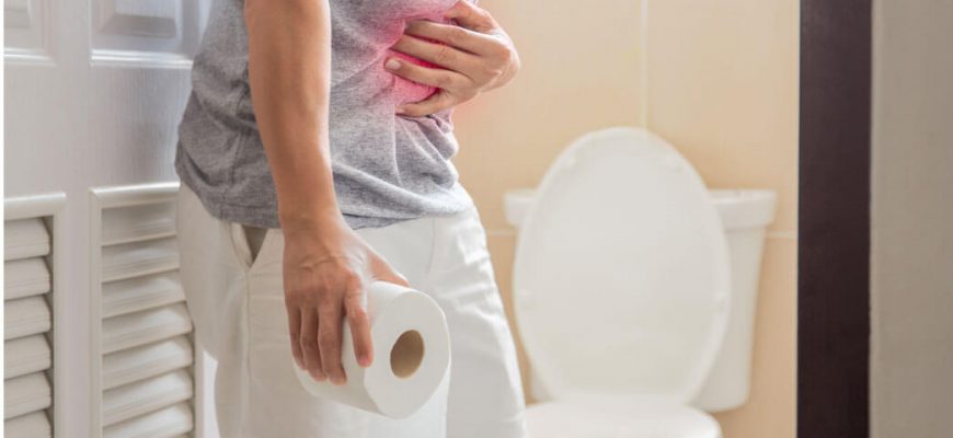 Man holding his stomach and a toilet roll outside a restroom, suggesting diarrhea treatment with Xifaxan