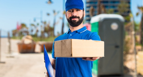 Delivery man dressed in blue holding a parcel in one hand and a folder in the other, facilitating prescription home delivery.