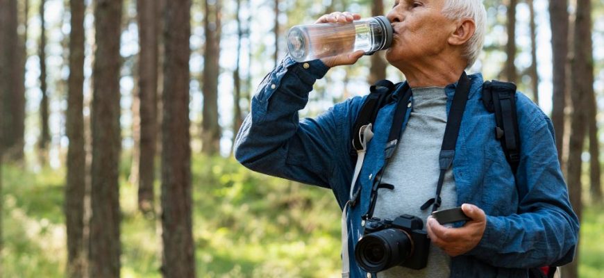 Senior man hydrating in the woods with a water bottle, combating overactive bladder.
